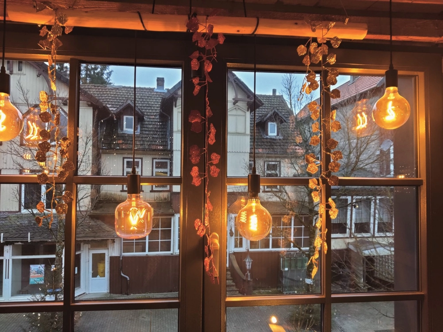 Reiselust Hahnenklee – Ferienhaus – Ein gemütliches Interieur mit Pendelleuchten im Industriestil mit großen Edison-Glühbirnen und künstlichen Ranken oder Grünpflanzen.