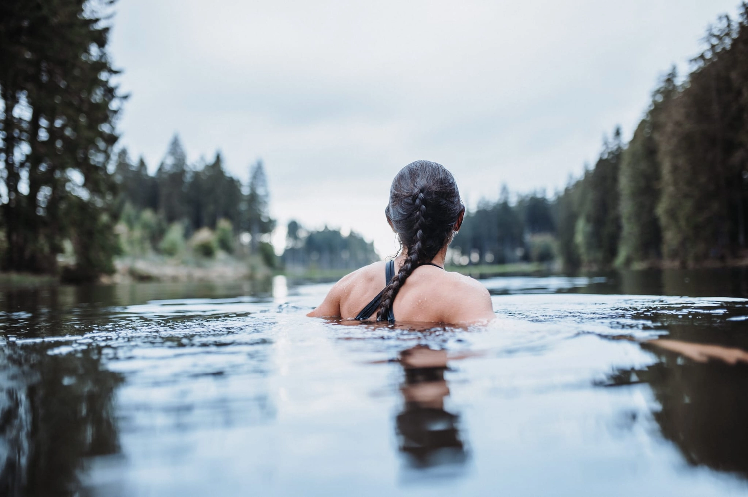 Reiselust Hahnenklee – Ferienhaus – eine Person schwimmt in einem malerischen, von Bäumen umgebenen See, eine Aktivität, die oft mit Schwimmen in freier Natur oder im offenen Wasser in Verbindung gebracht wird.